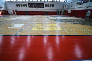 Applying multiple coats of finish on hardwood gym floors to extend durability and protect flooring investment
