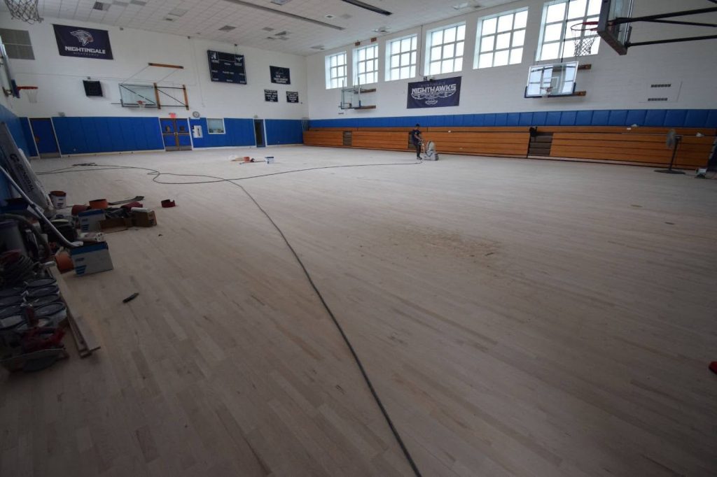 Flooring team sanding and refinishing school basketball court