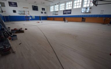 Flooring team sanding and refinishing school basketball court