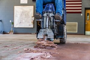 RM crew member repairing a school gym floor as part of multi-phase flooring projects