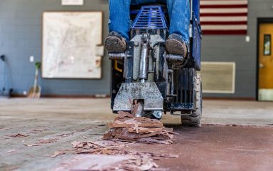 RM crew member repairing a school gym floor as part of multi-phase flooring projects